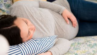 How should you sleep during pregnancy? Image shows pregnant woman sleeping holding baby bump