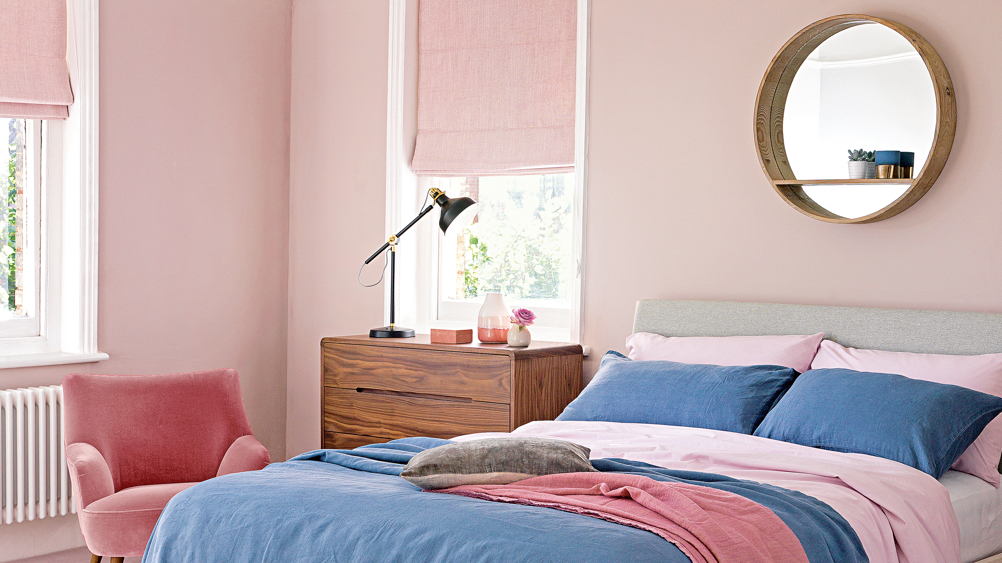 A pink bedroom with blue accents and a bedroom mirror above the bed