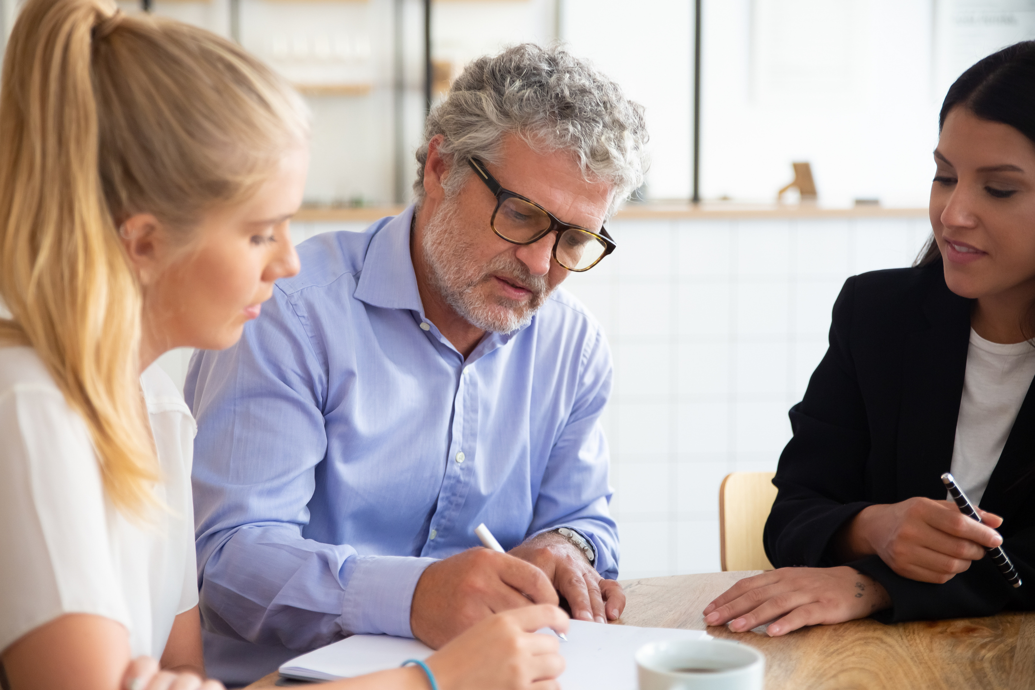 Focused young and mature customers meeting with agent and signing insurance agreement. Group of business people at co-working. Business meeting concept