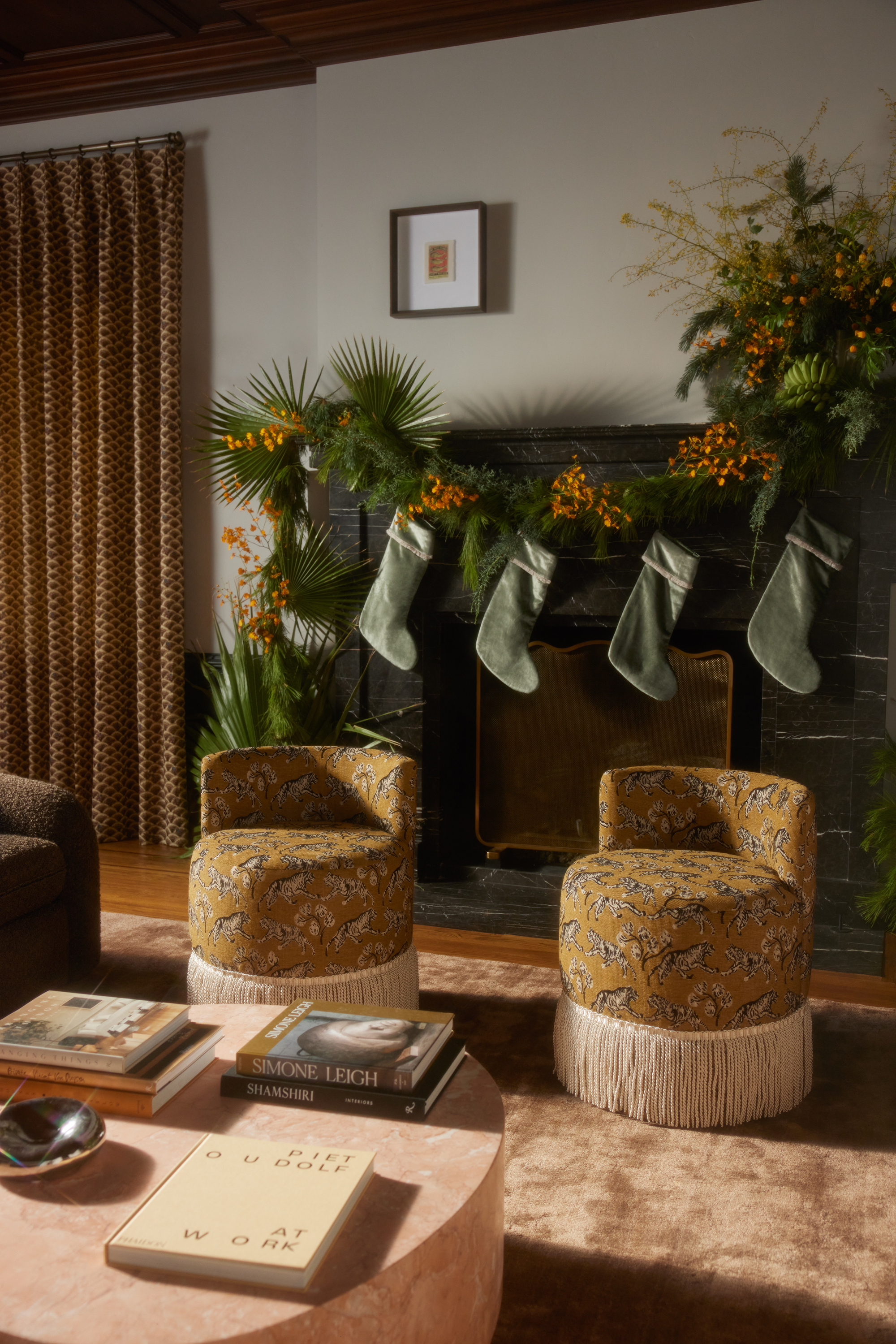 A living room fireplace decorated for Christmas with two patterned accent chairs with fringing