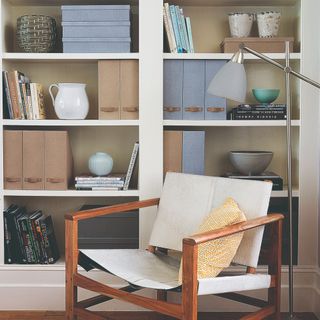 A built-in bookcase filled with books and decorative objects with an accent chair in front of it