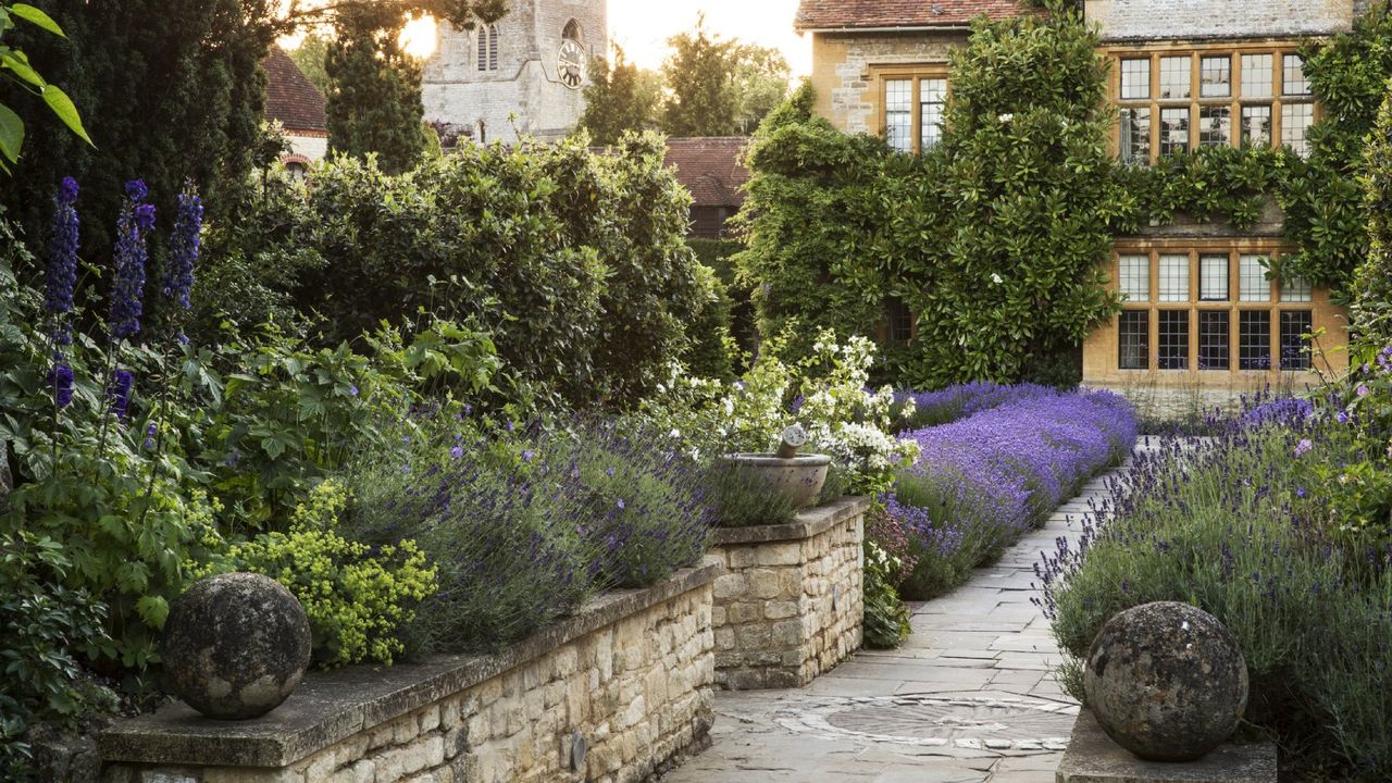 A mature flowerbed along a stone walkway leading to a house