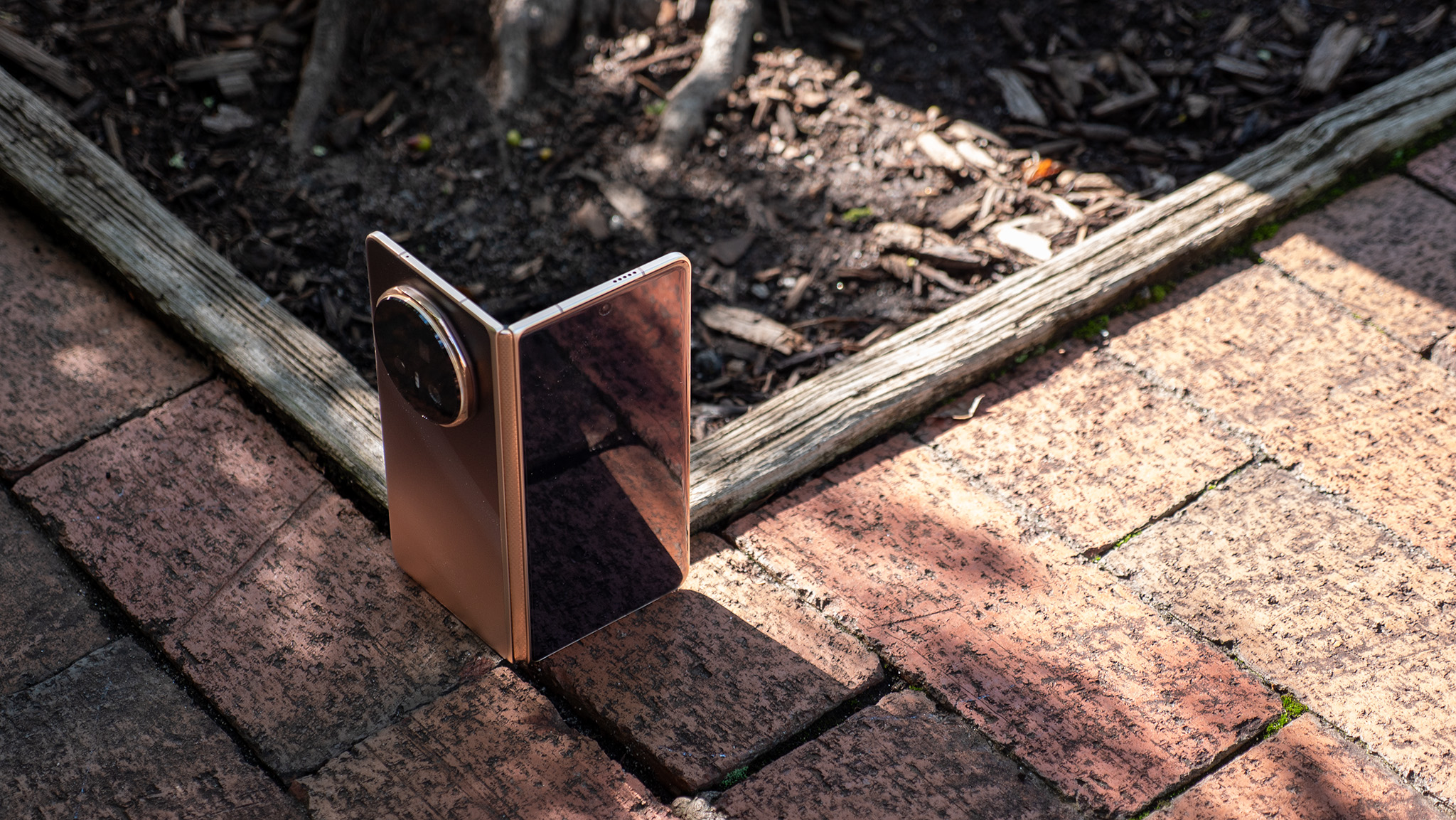 The gold Honor Magic V5 tented vertically in front of a garden bed