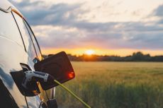 An electric car plugged in against a background of a rural location at sunset