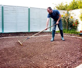 A man raking soil to prep an area in a garden for laying turf
