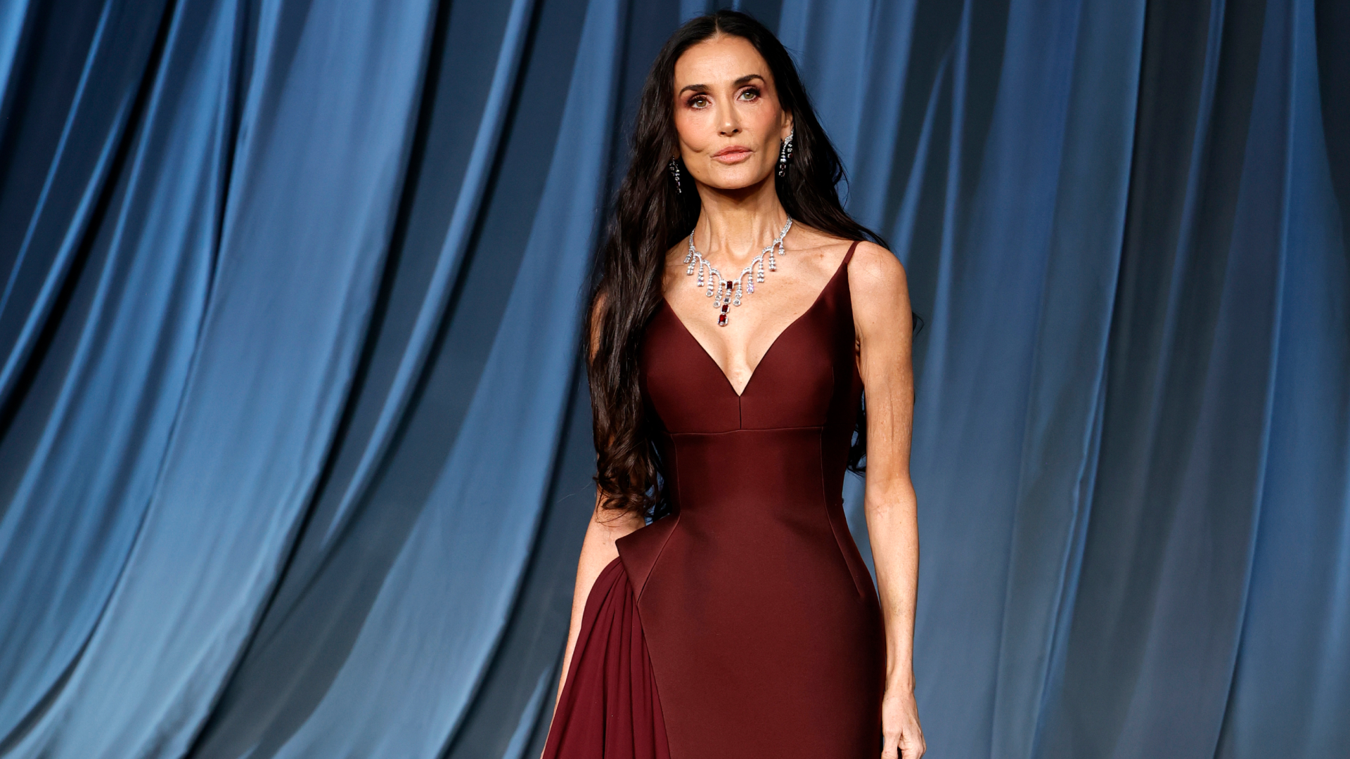 Demi Moore wearing a burgundy spaghetti strap dress.