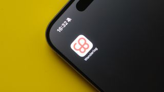 Wanderlog app logo on an iPhone 15 Pro Max with yellow background