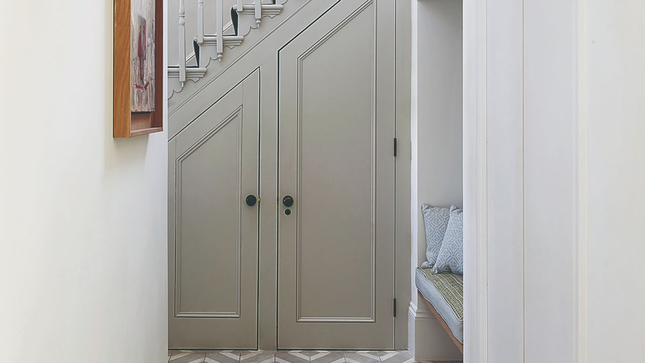 Grey under stairs cupboard with tiled floor and built-in bench.