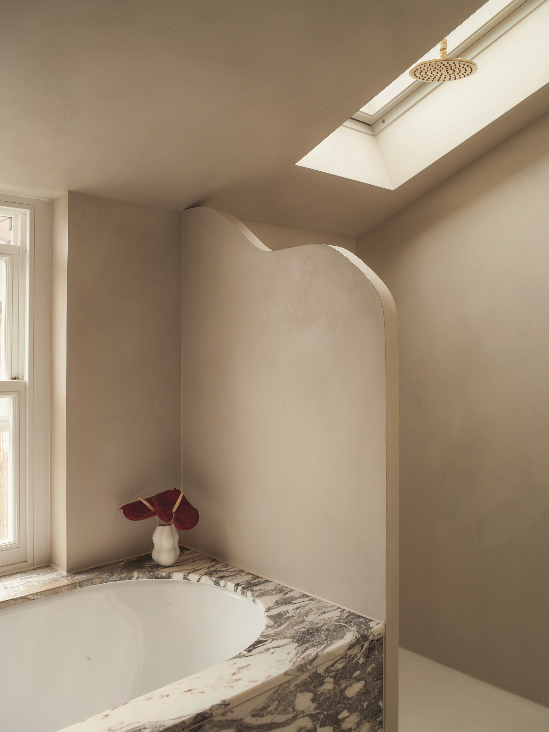 a minimalist bathroom with a shower wall, marble bath and shower head in a roof light