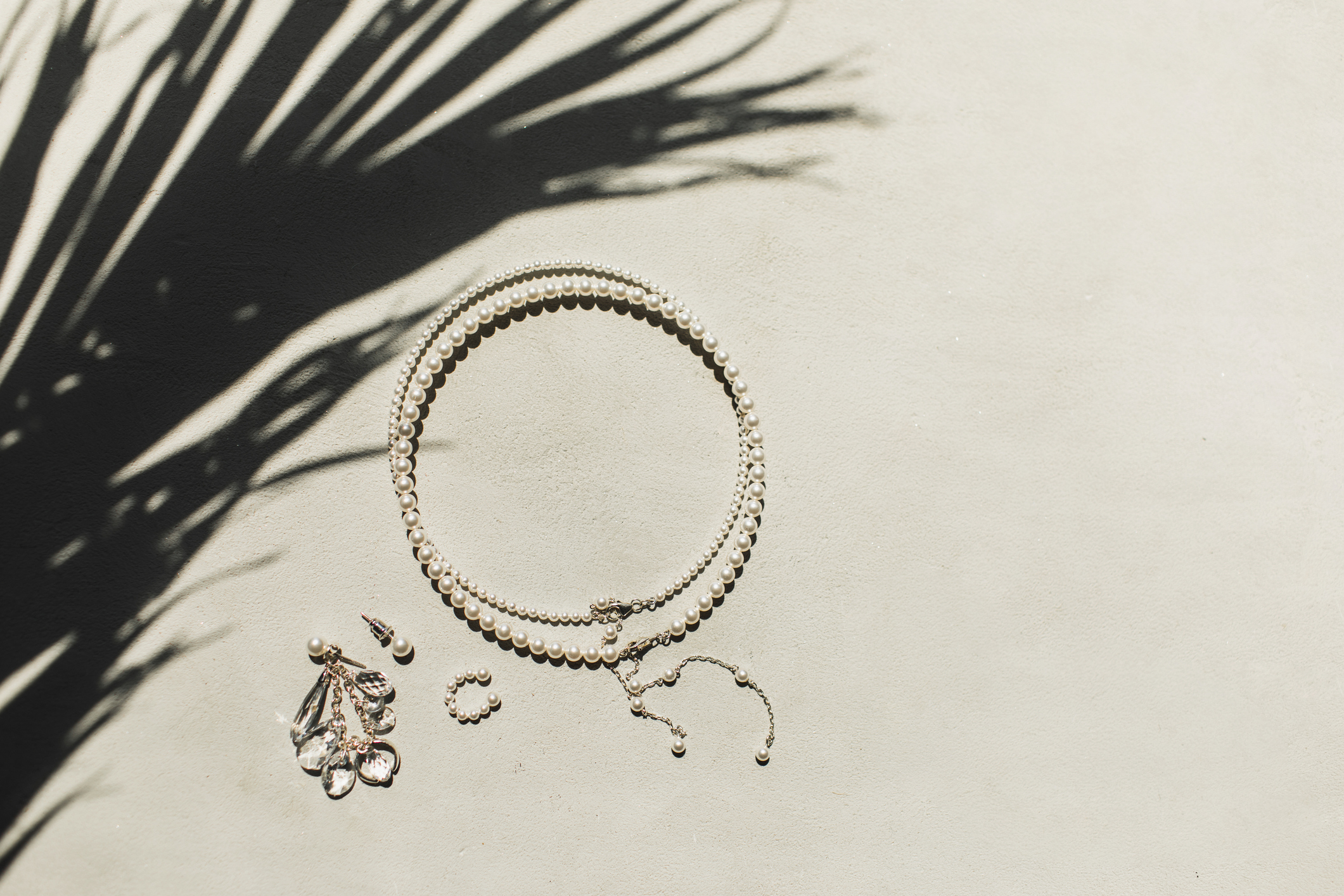A silver pearl bracelet and earrings on a sandy backdrop in the sun.