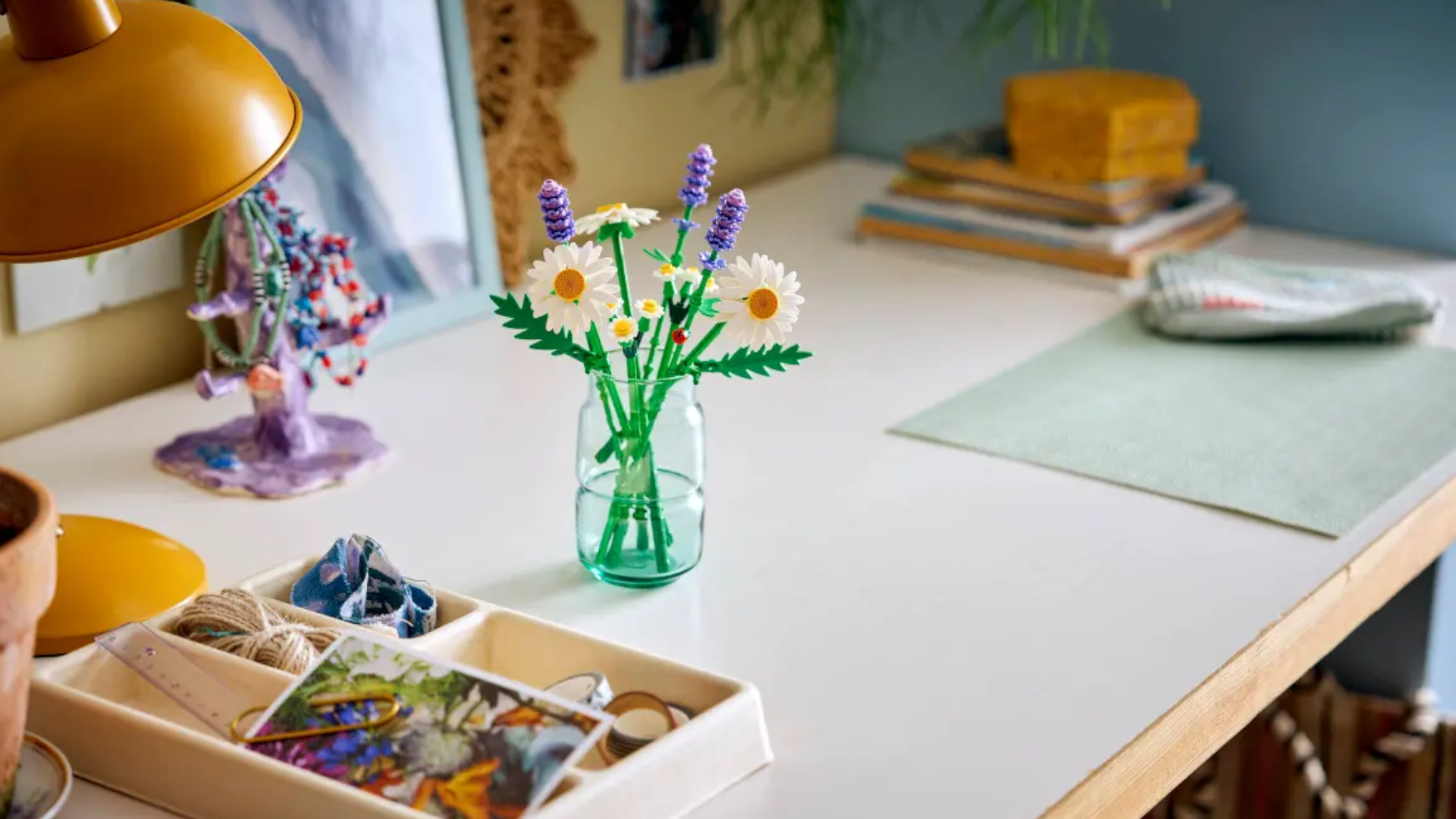 Lego Daisies in a glass jar on a desk with craft pieces lying in storage on it