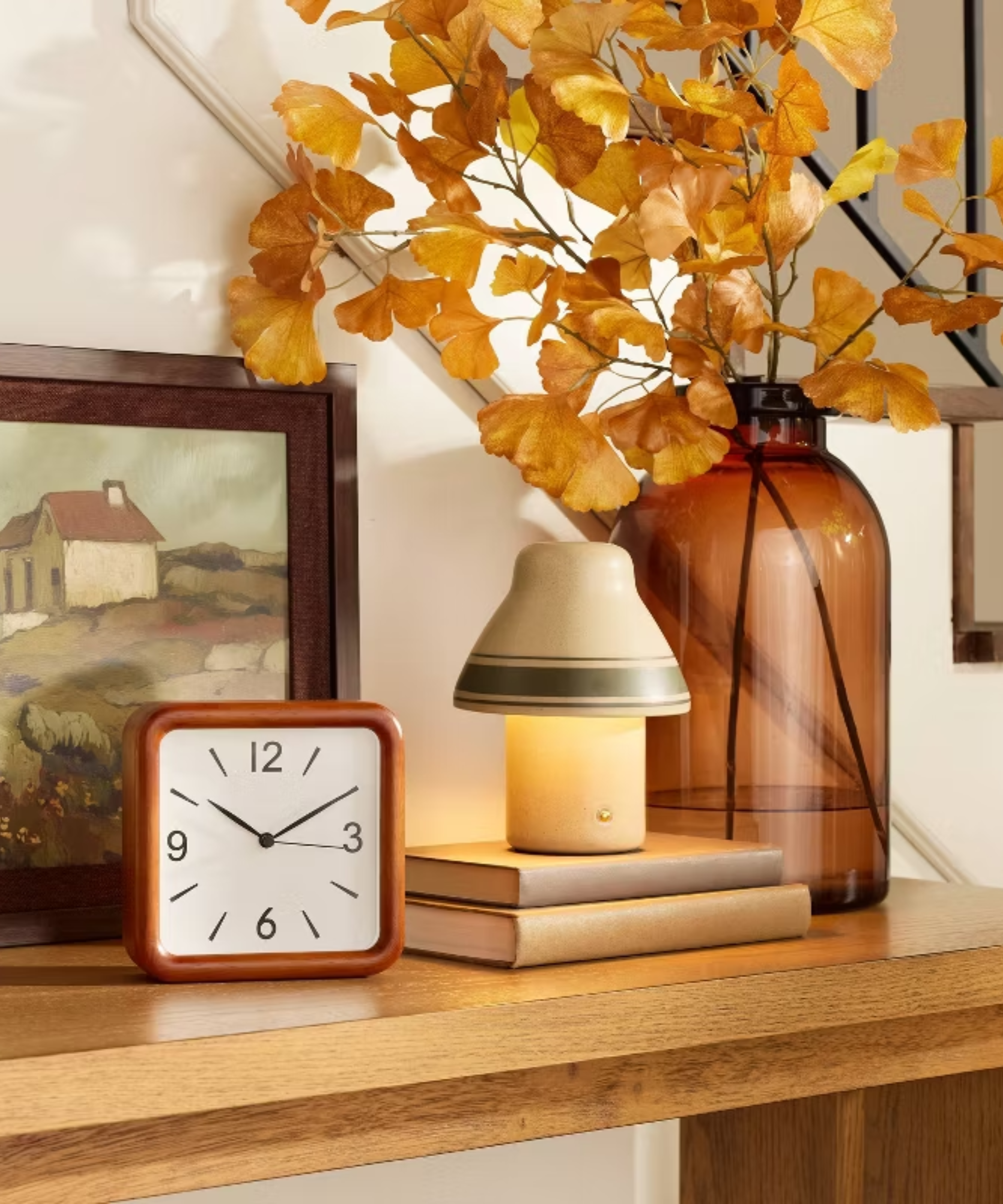 a fall vignette with a small lamp, a clock, books, and a large vase