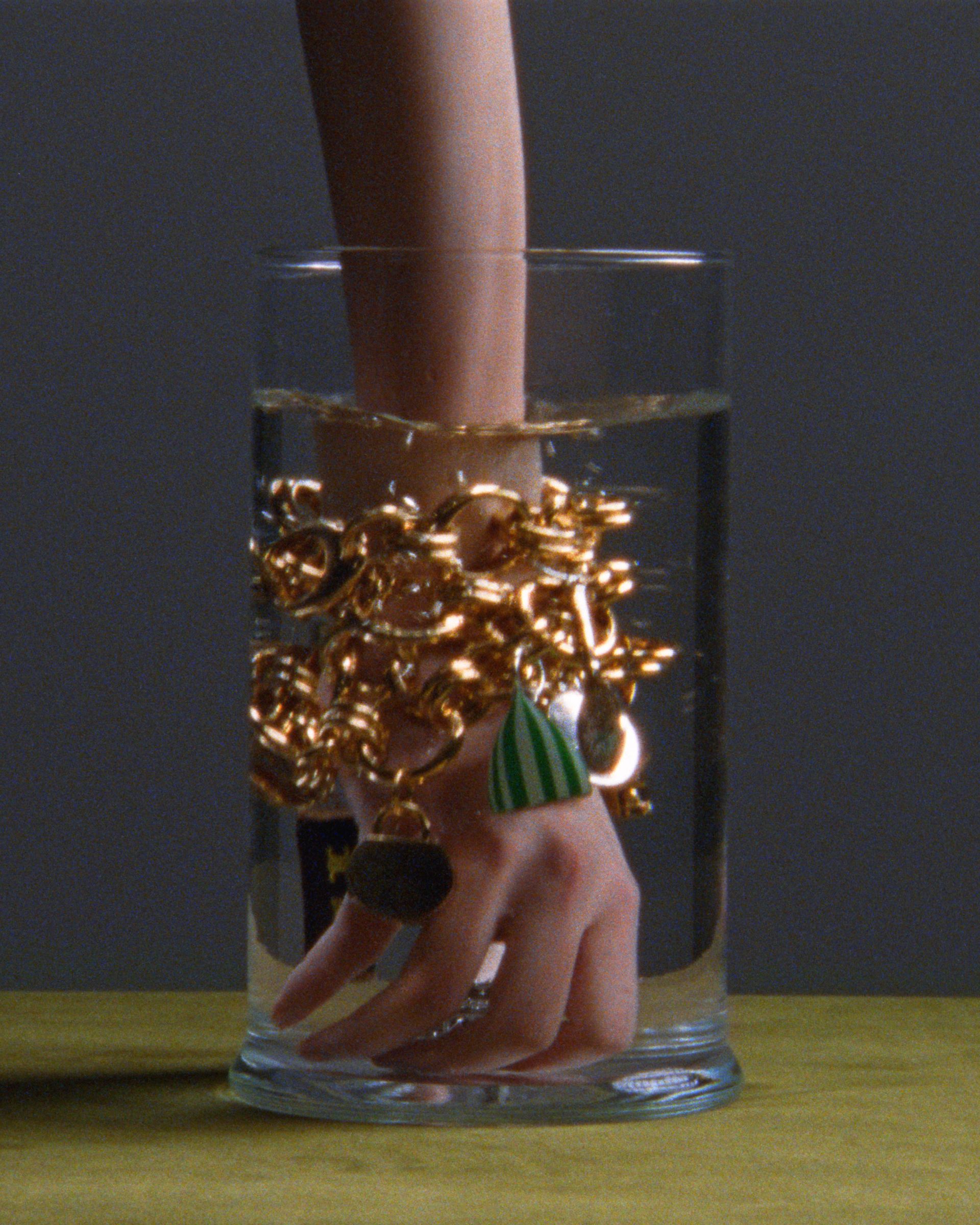 Celine charms on a bracelet worn by a person sticking their hand in a glass of water.