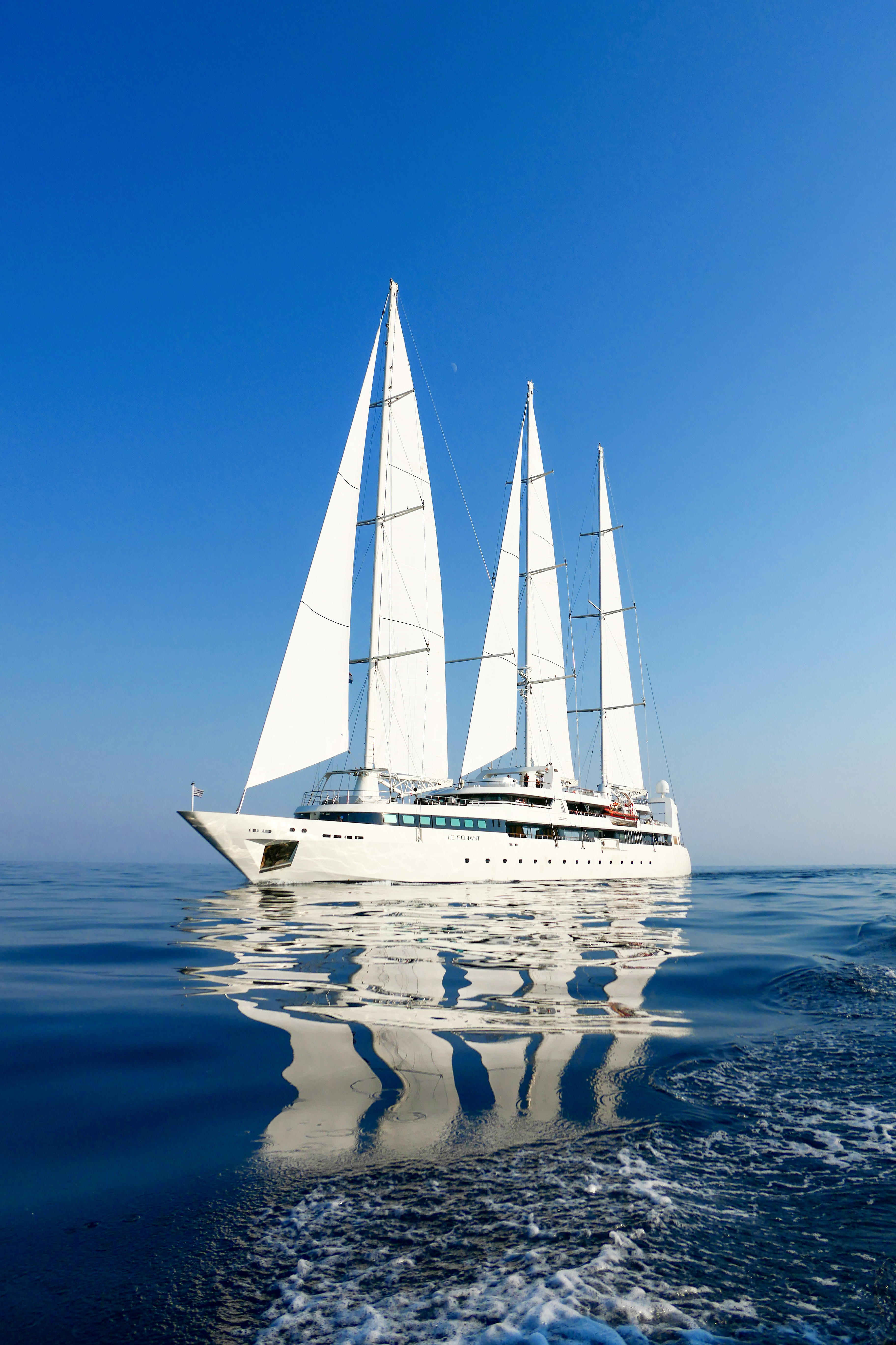 White boat with five white sails reflected in dark blue water