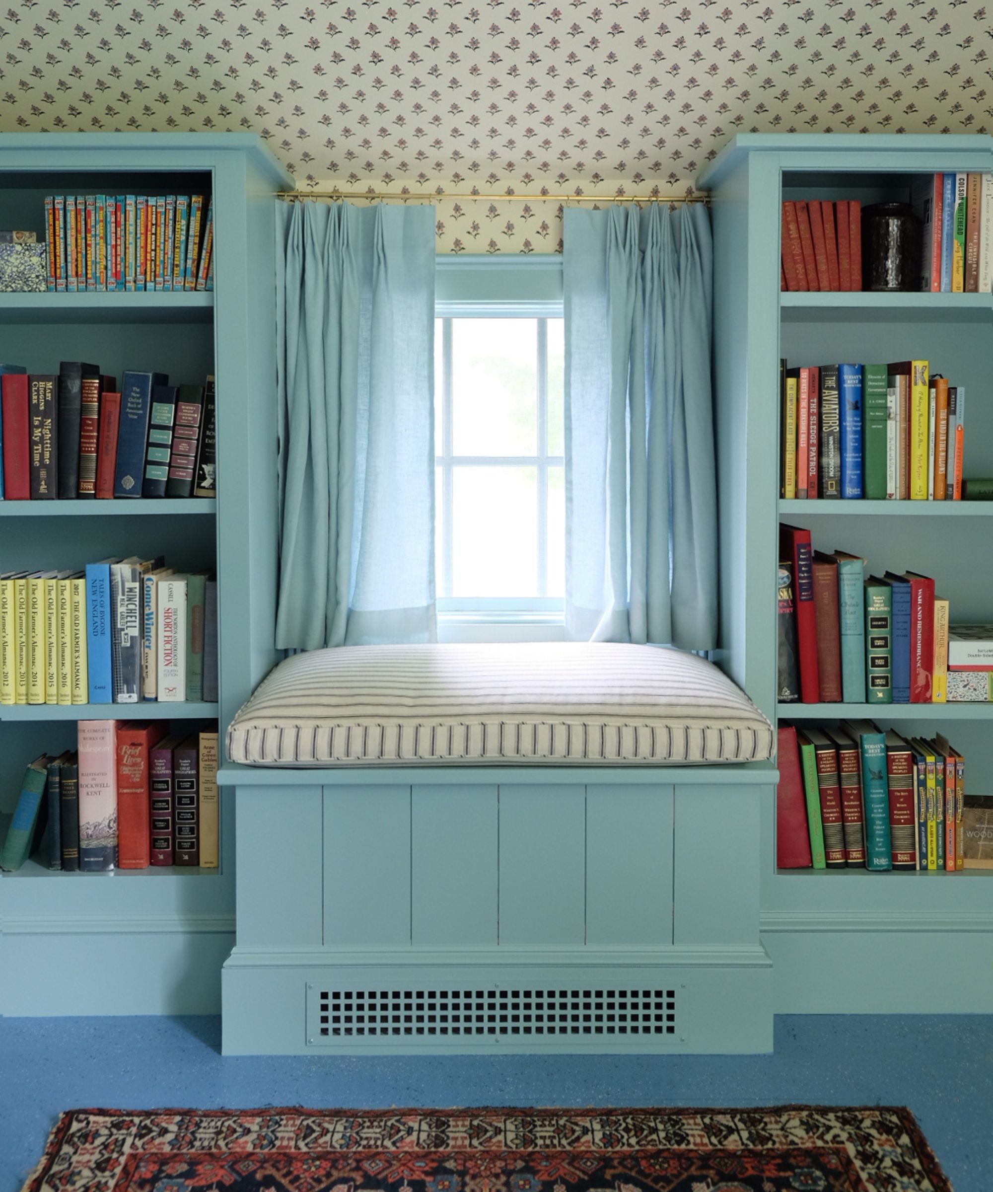 a light blue reading nook built around a small window with a ditsy floral wallpaper, window seat, and a blue painted floor