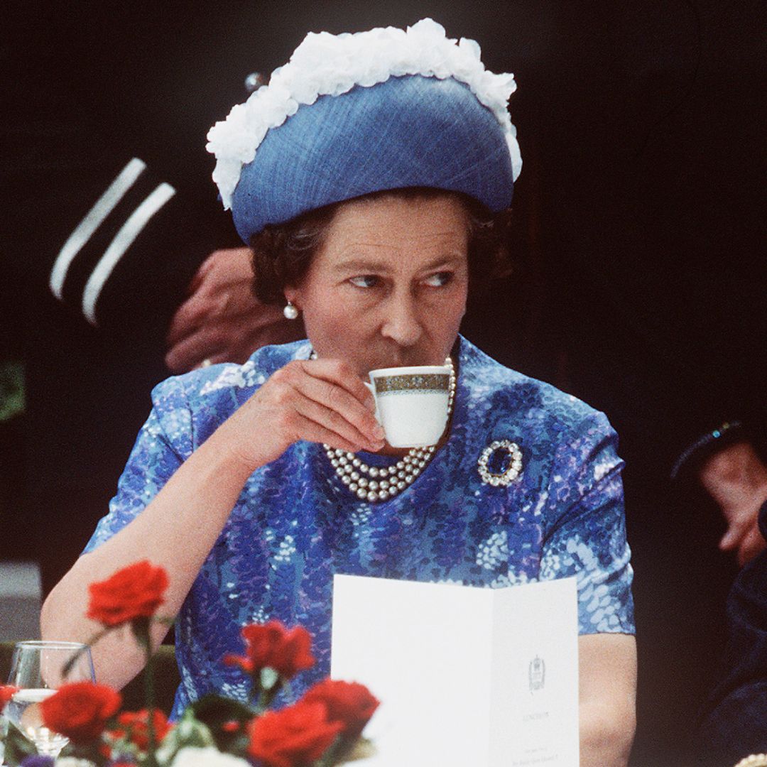 Queen Elizabeth wearing a blue dress and hat drinking tea