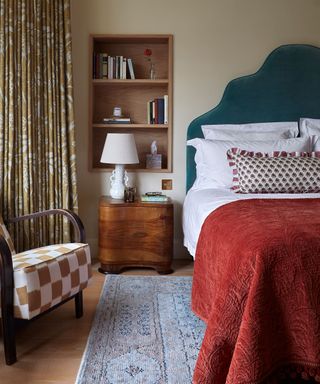 cozy bedroom with a large bed with blue headboard and red throw blanket with a storage niche in the wall