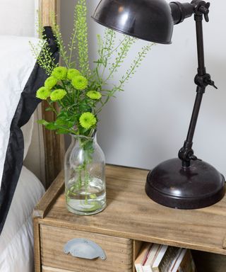 Green flowers in vase next to bed with black Lamp