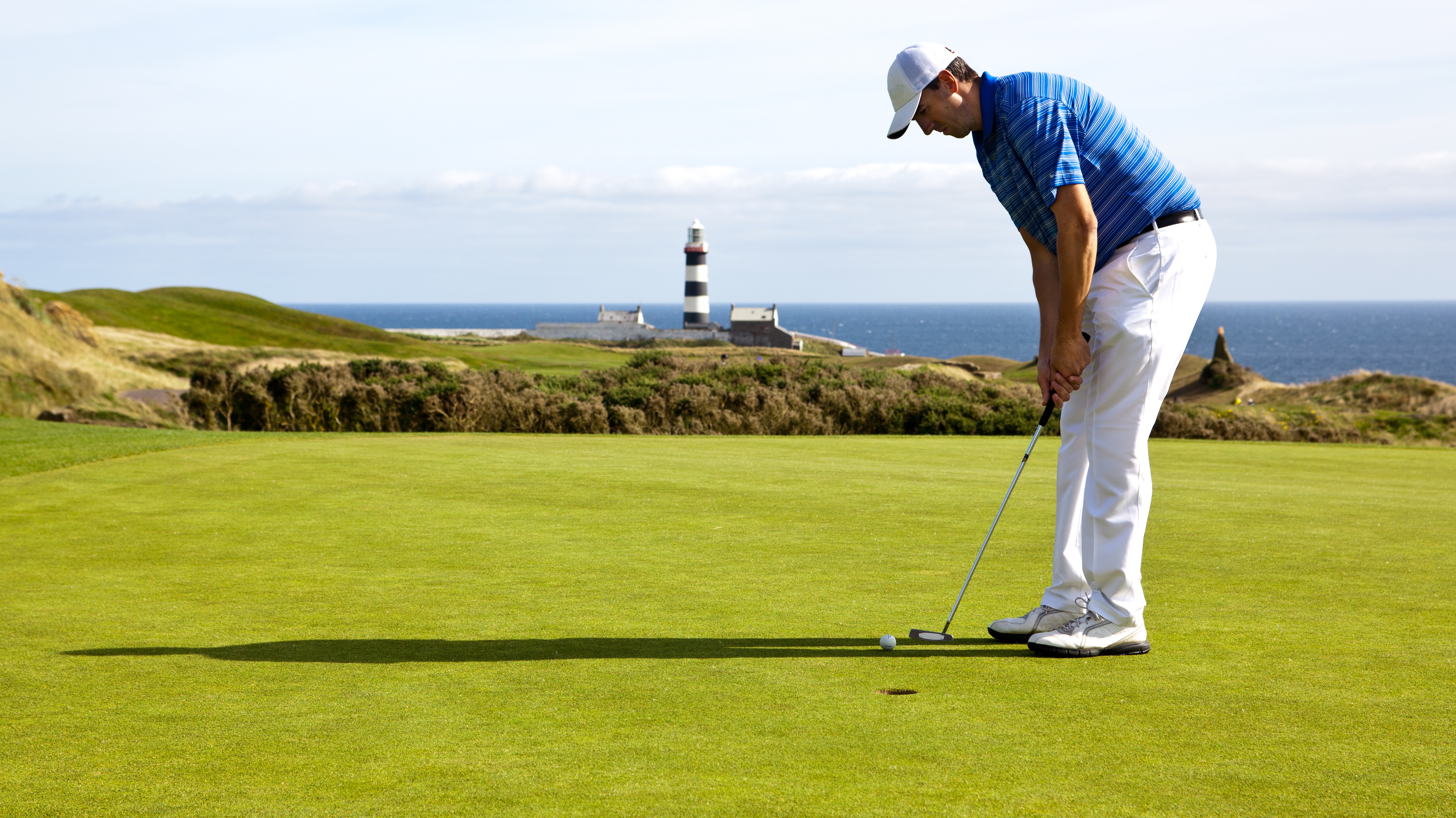 A golfer putts at Old Head with the lighthouse in the background