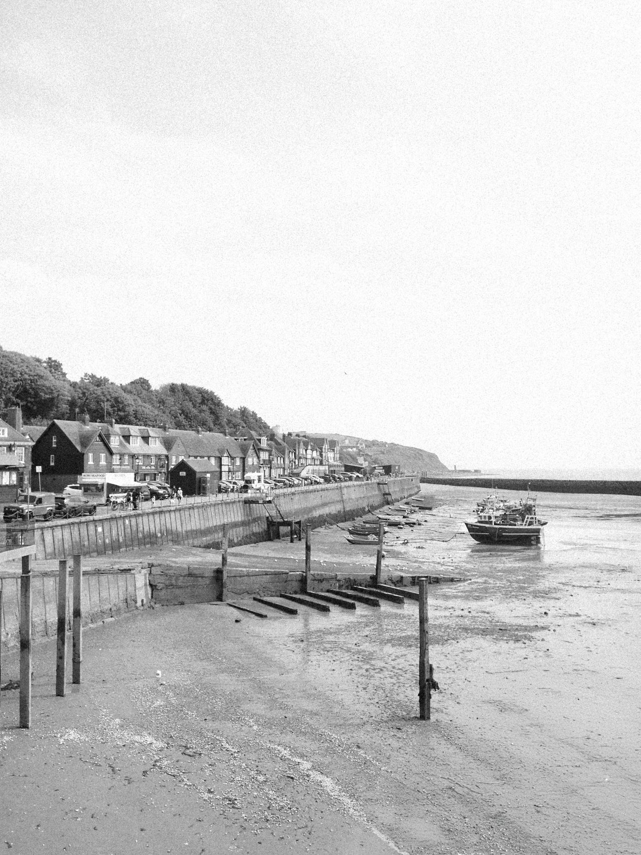 A seafront path with houses and fishing boats while the tide is out