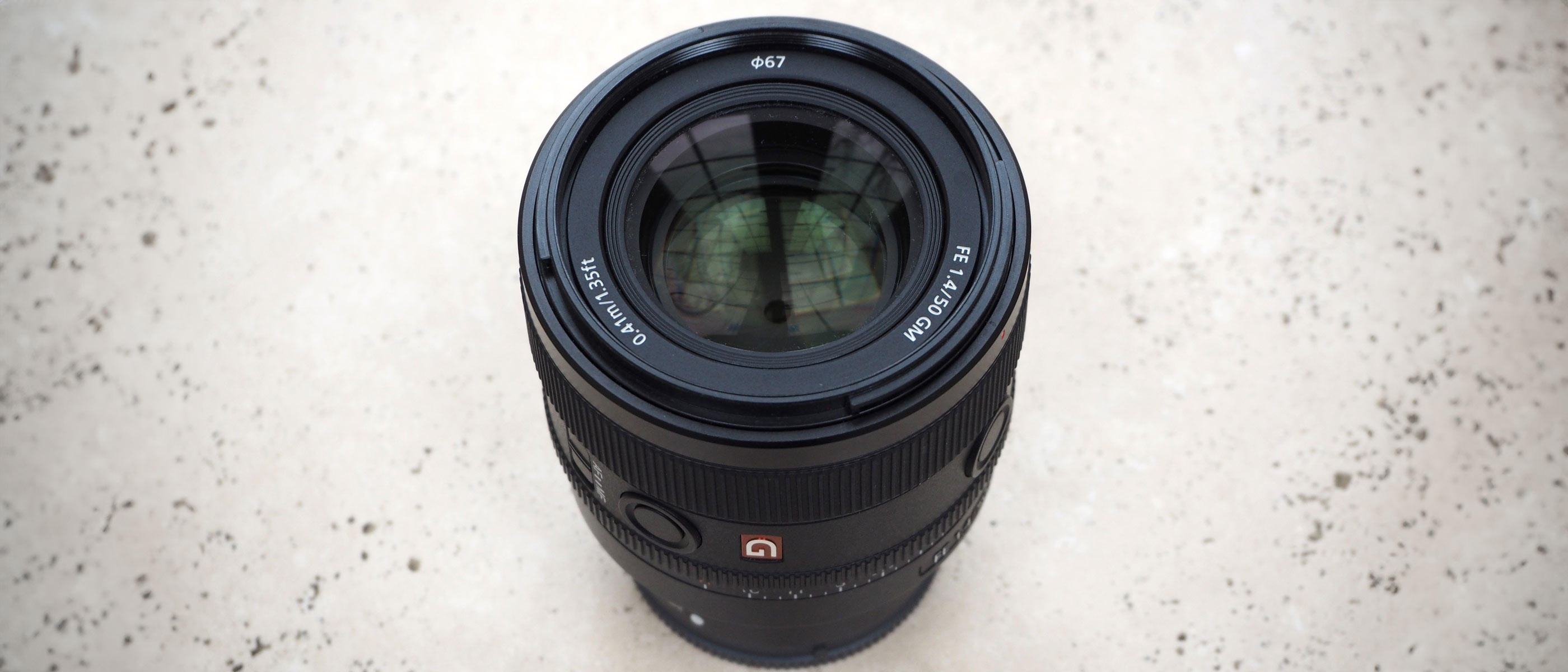 A Sony 50mm f/1.4 GM lens standing on a table with the optical elements showing.