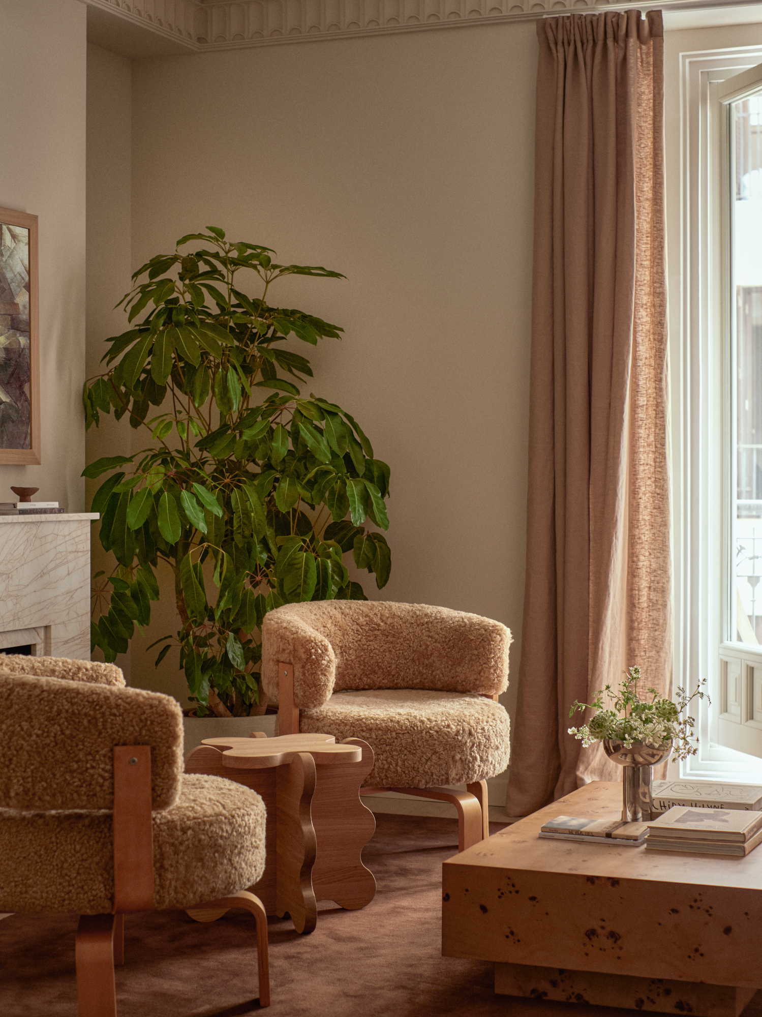 Corner of a living area with rust carpet, burl wood coffee table, beige sheepskin and wood accent chairs and a wiggly wood side table