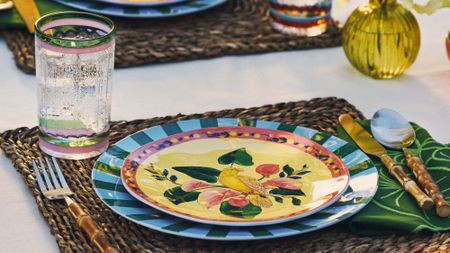 Pattern-drenched tropical tableware styled alfresco alongside bamboo-handled cutlery