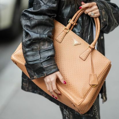 Woman wearing a glossy manicure holding a Prada tote bag