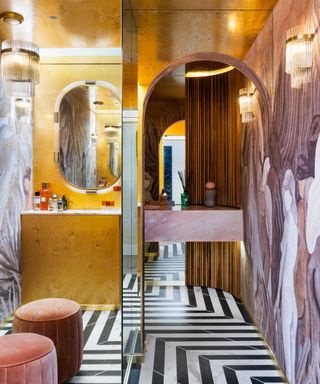 A bold powder room with black a white striped tile flooring, antiqued metallic walls and round mirrors