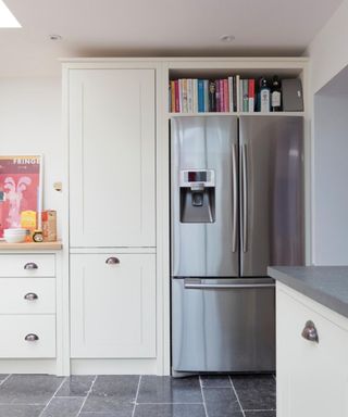 White kitchen units, black floor tiles, large fridge freezer with cookbooks on it