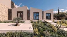 A Greek villa with a flourishing garden bordering the entryway and a dwarf olive tree in the middle