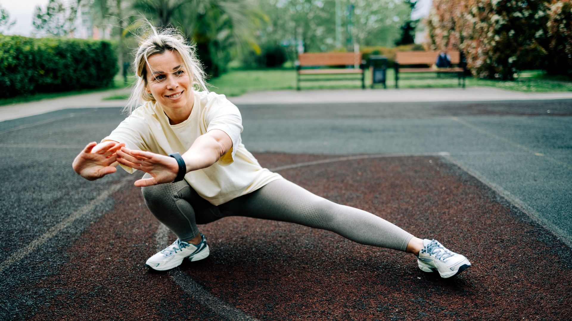 Woman doing functional fitness exercises in park wearing workout clothes, smiling