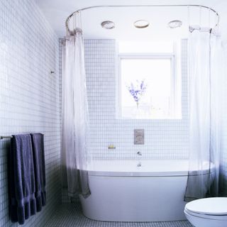 A white tiled bathroom with blue accents and a high shower curtain rod