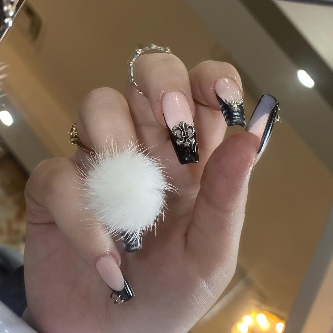 a person wearing coffin nails with black tips and nail charm attachments