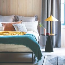 A wall-panelled bedroom with a yellow table lamp on the bedside table next to the bed