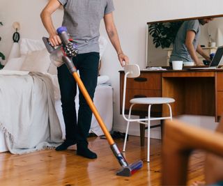 A man using a Dyson vacuum to clean a wooden floor.
