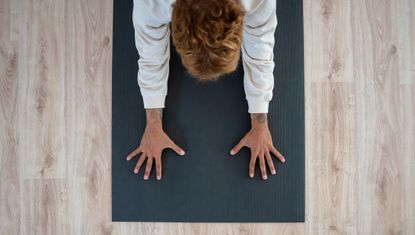 Aerial view of man spreading his fingers on a yoga mat. He is wearing a white sweatshirt. 