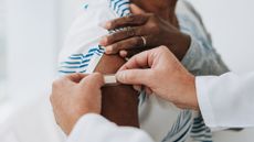 close up on an older woman's arm as male doctor places a bandage on it, as if she's just received a vaccine