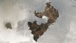 An astronaut photo of two islands with a silver mirror-like ocean surface caused by a sunglint