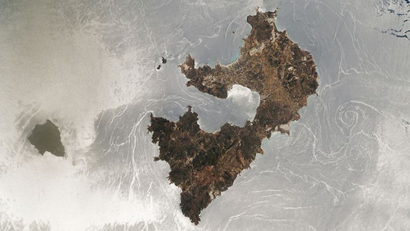 An astronaut photo of two islands with a silver mirror-like ocean surface caused by a sunglint