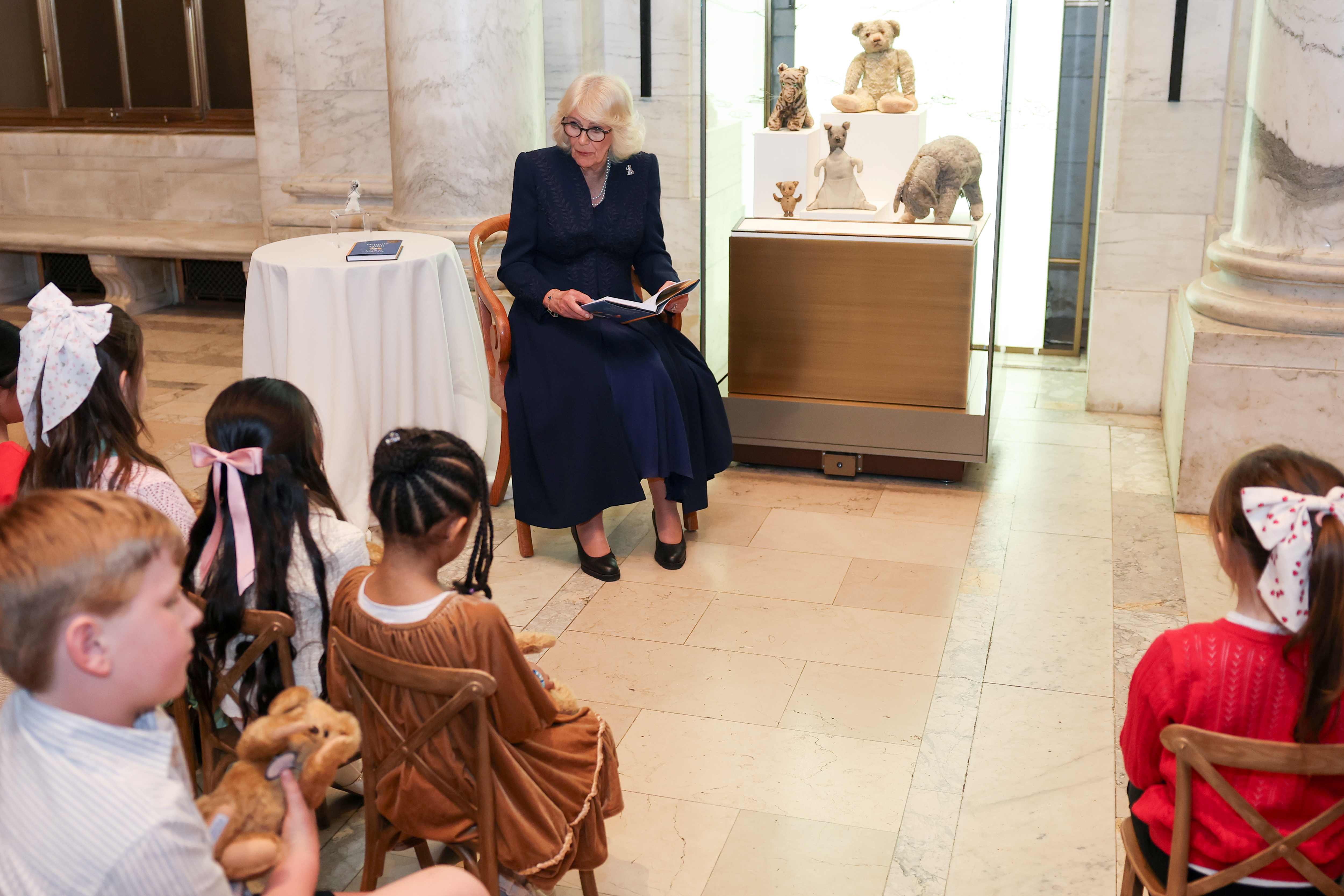 Queen Camilla reading to school kids in front of a case of teddies