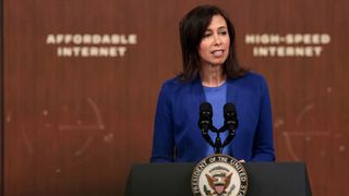 Jessica Rosenworcel stands before a presidential podium, dressed in a blue suit with the blurred words 'Affordable Internet' and 'High Speed Internet' in the background