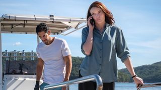 Mack on the phone standing by Greg on a boat