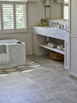 A bathroom with a marble vanity and patterned floor tiles framing the bathtub