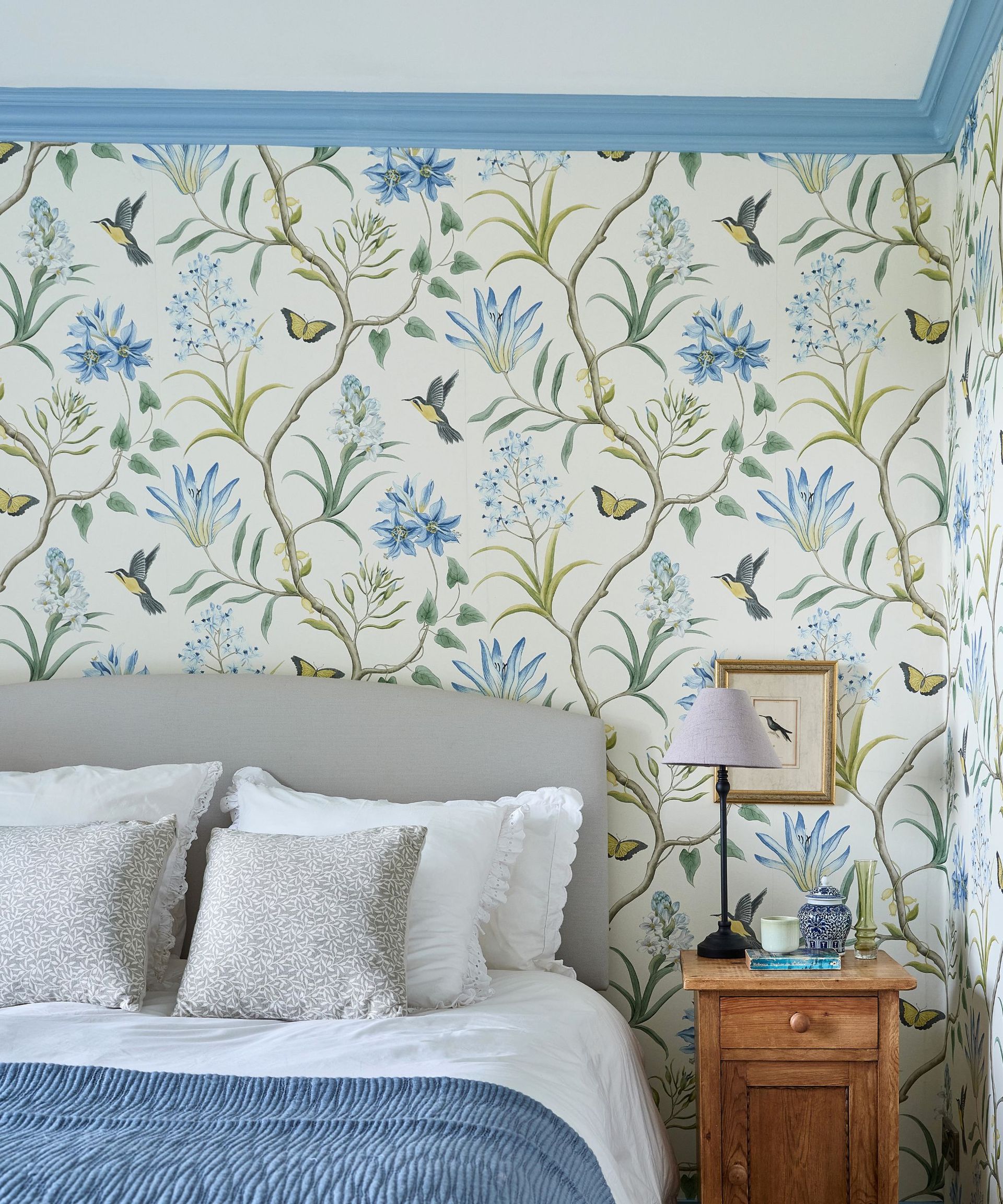 Romantic bedroom with floral wallpaper white bedding, blue throw and grey cushions