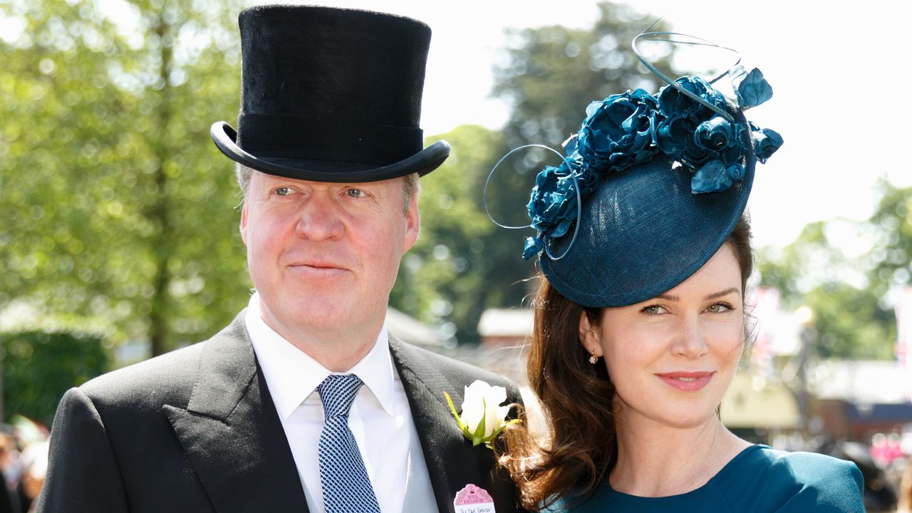 Charles Spencer wearing a top hat and suit standing next to Karen Spencer in a blue dress and matching hat with flowers