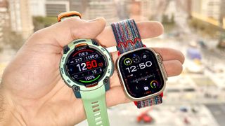 Close-up of the Garmin Instinct 3 next to the Apple Watch Ultra 3 with the Barcelona skyline in the distance