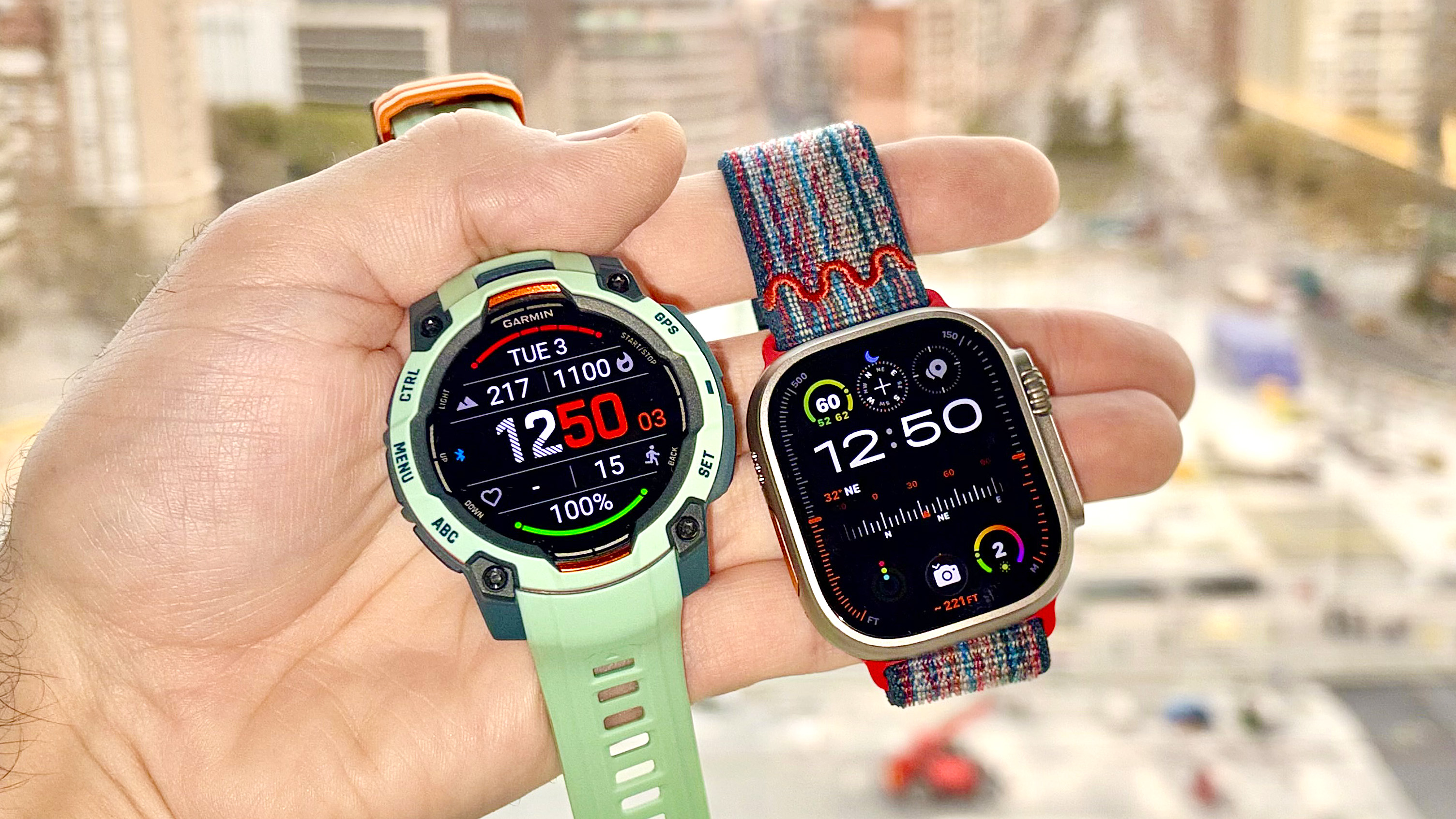 Close-up of the Garmin Instinct 3 next to the Apple Watch Ultra 3 with the Barcelona skyline in the distance