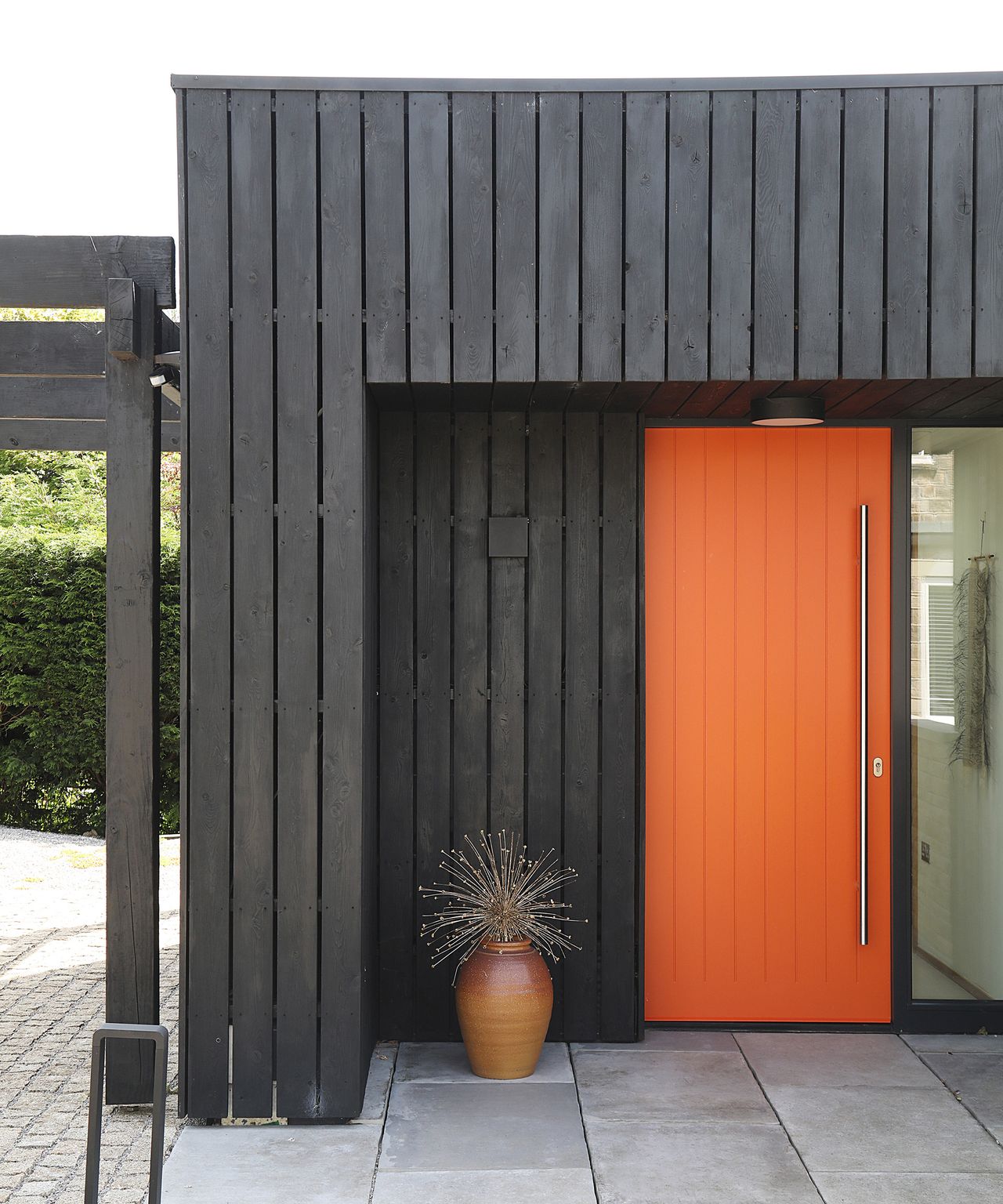 An orange front door set into a black clad contemporary home