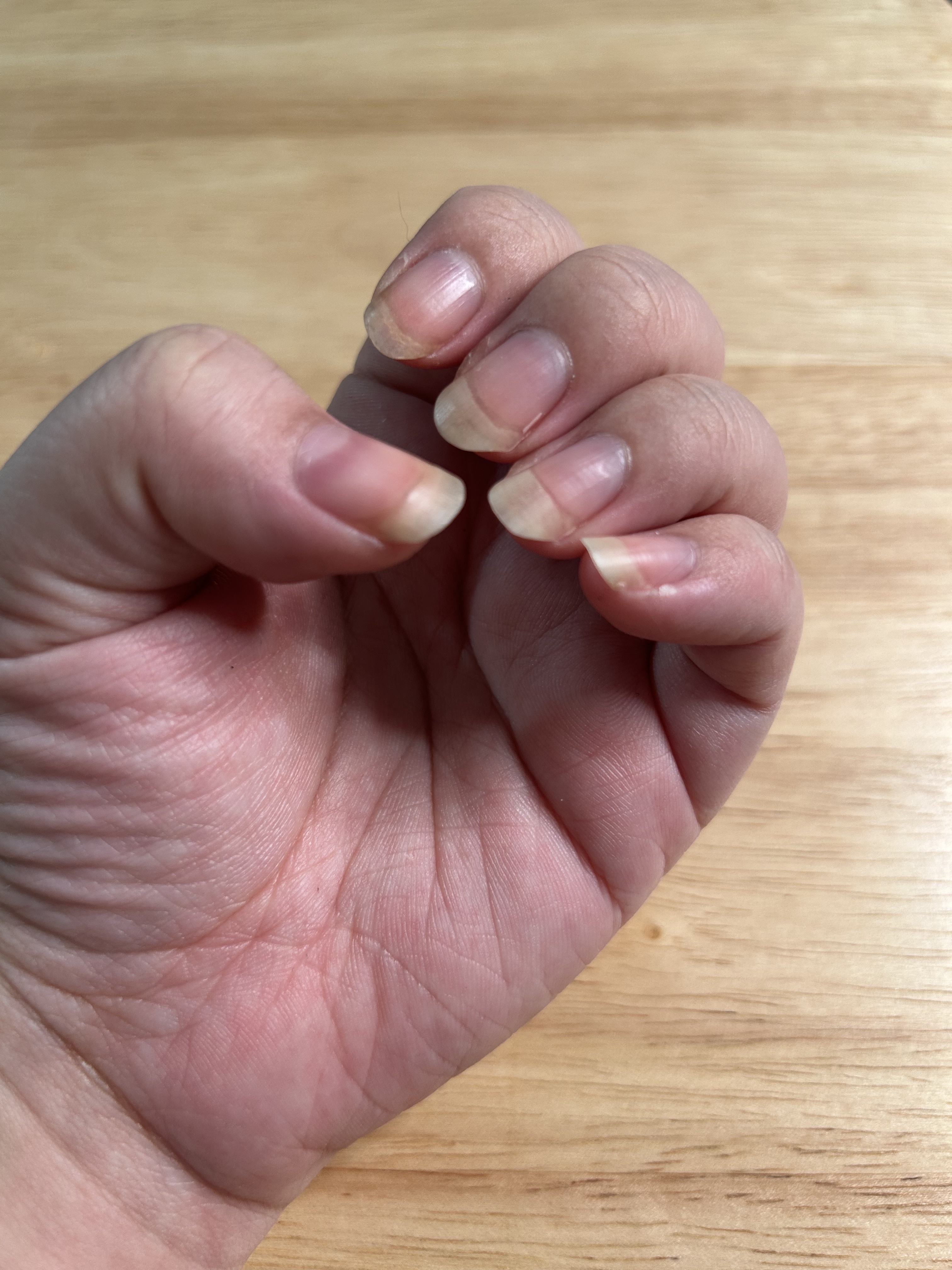A woman's hand and nails before applying cuticle oil with a wood background.